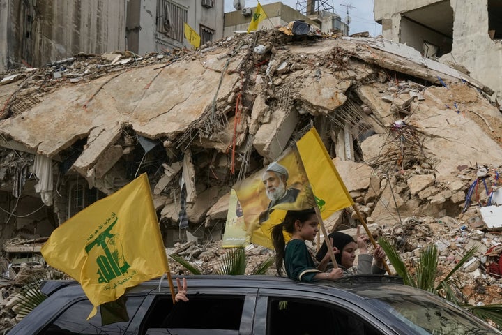 Displaced residents wave Hezbollah flags, including one bearing a picture of its leader, Naim Qassem, as they pass rubble of destroyed buildings in Dahiyeh, Beirut's southern suburbs, Lebanon on April 17, 2026, following a ceasefire between Israel and Hezbollah.