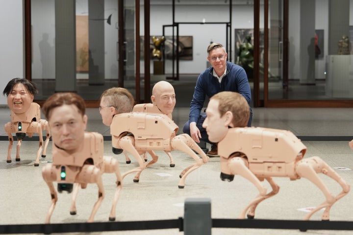 Artist Beeple, Mike Winkelmann, poses inside his installation titled "Regular Animals," with robots in the likeness of Kim Jong Un, left, Elon Musk, second from left, Jeff Bezos, center, and Mark Zuckerberg, right, at the Neue Nationalgalerie museum in Berlin, Germany.
