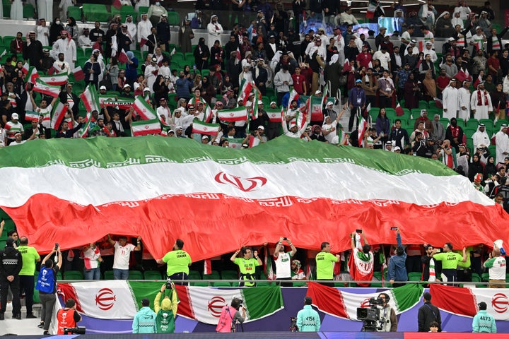 Iran fans hold their country's giant national flag during the Qatar 2023 AFC Asian Cup semi-final football match between Iran and Qatar at al-Thumama Stadium in Doha in February 2024.