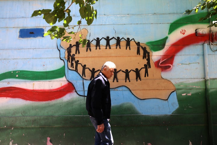 An Iranian man walks past the map of Iran, with its citizens holding hands, painted on a wall in the capital Tehran on May 9, 2026. Iran questioned the seriousness of American diplomacy on May 9, in the wake of renewed naval clashes in the Gulf, while keeping Washington waiting for a response to its latest negotiating position. On February 28, 2026, Israel and the United States launched strikes on Iran, killing its supreme leader and triggering a war that spread across the Middle East. (Photo by ATTA KENARE / AFP via Getty Images) / 