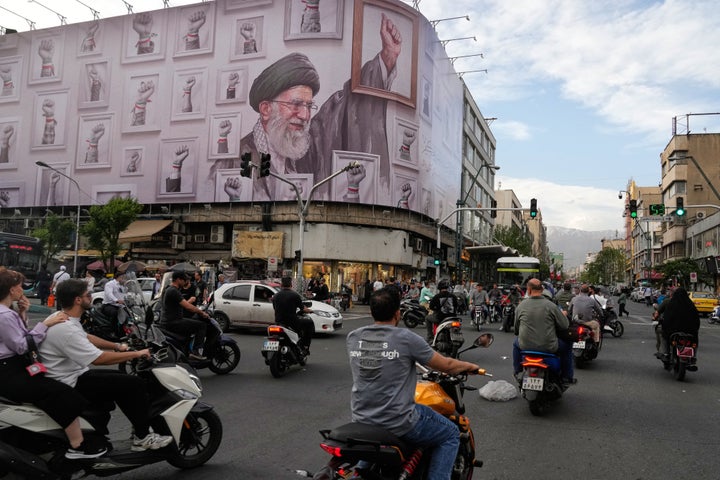 Motorbikes drive past a billboard with graphic showing the late Iranian Supreme Leader Ayatollah Ali Khamenei, who was killed in the U.S. and Israel strikes on Feb. 28, with his framed fist amongst his supporters framed fists in downtown Tehran, Iran, Wednesday, May 6, 2026. (AP Photo/Vahid Salemi)
