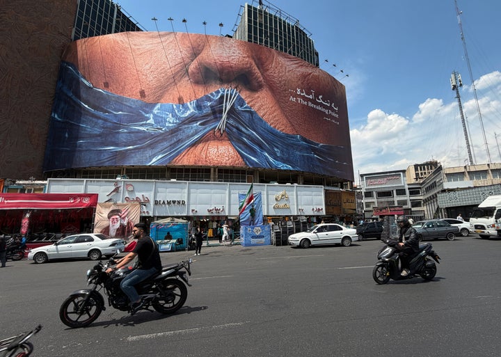 Vehicles pass a billboard with graphics depicting the Strait of Hormuz and U.S. President Donald Trump's sewn lips in a square in downtown Tehran, Iran, Saturday, May 2, 2026. (AP Photo/Vahid Salemi)