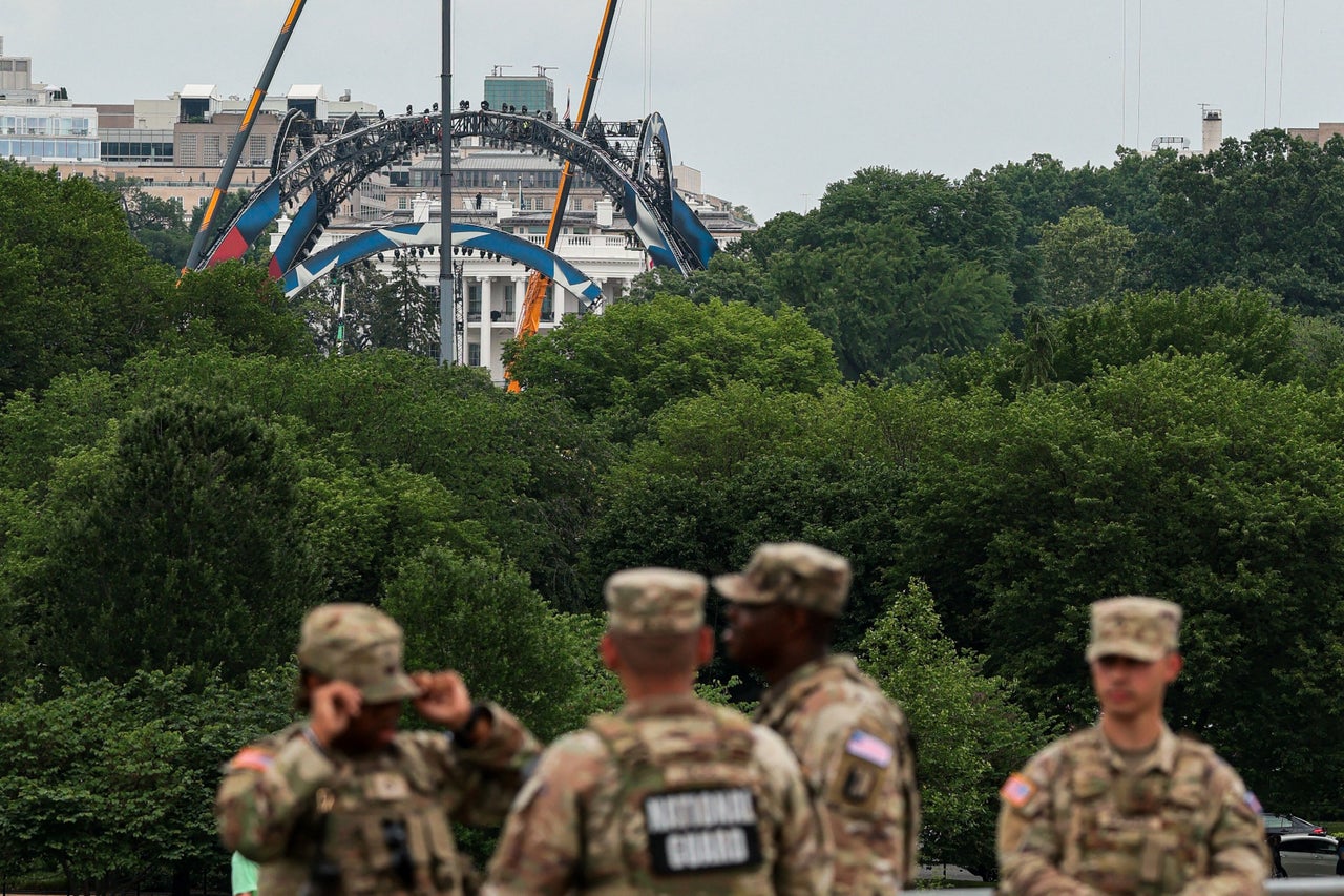 Members of the National Guard stand at the base of the Washington Monument as construction on a temporary arena that will host the UFC Freedom 250 fight card in June on the South Lawn of the White House appears in the distance.