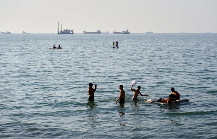 Residents swim and play in the waters of the Strait of Hormuz while cargo ships and commercial vessels lie anchored in the distance off Bandar Abbas, Iran, Wednesday, June 10, 2026.(Razieh Poudat/ISNA via AP)