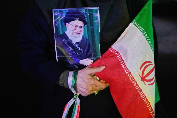 A demonstrator holds a poster of the slain Iranian Supreme Leader Ayatollah Ali Khamenei, who was killed in the U.S. and Israel strike on Feb. 28, and an Iranian flag during a pro-government gathering at a square in downtown Tehran, Iran, Tuesday, May 19, 2026. (AP Photo/Vahid Salemi)