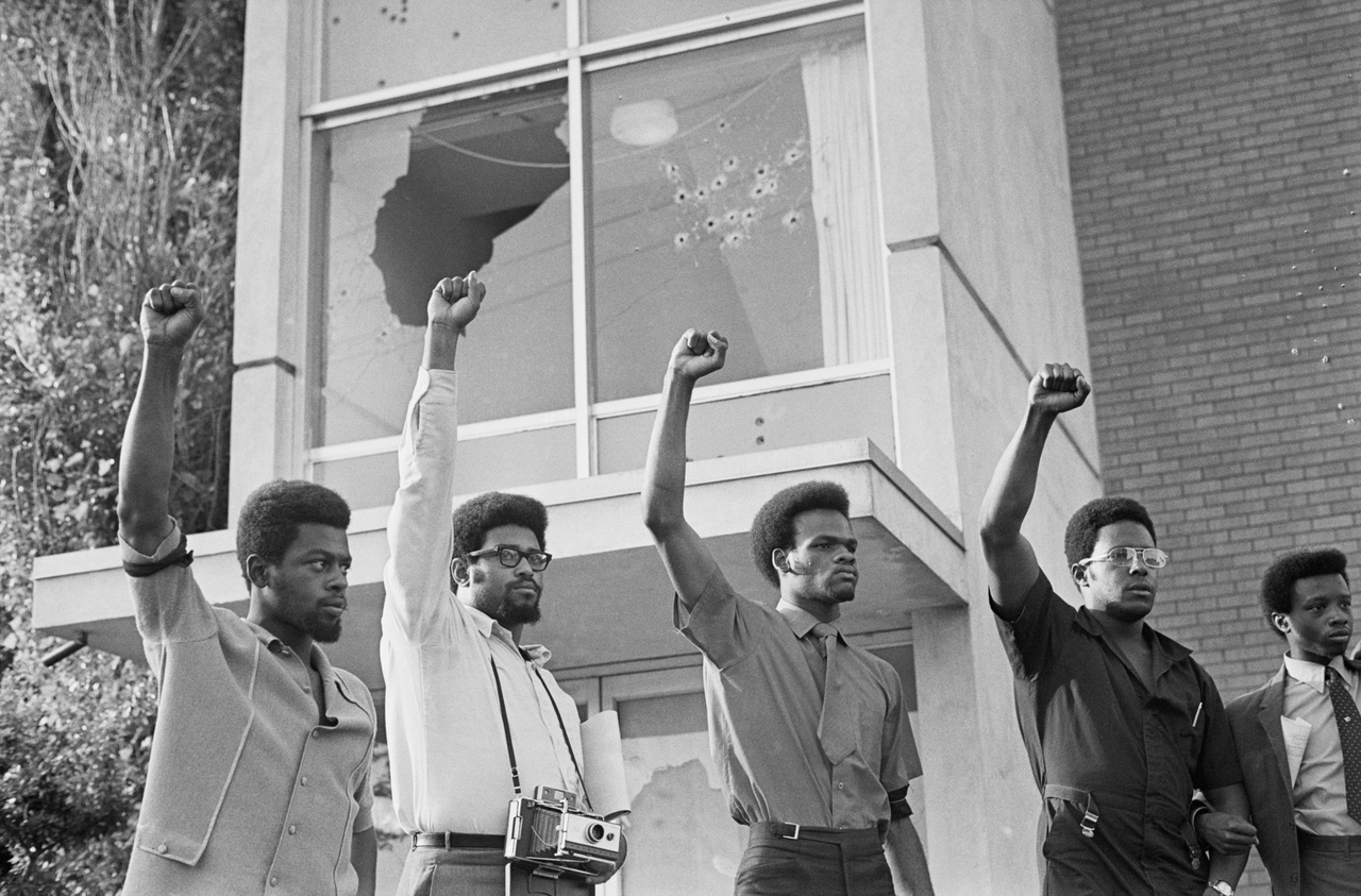 Bullet riddled Alexander Hall (a dormitory at Jackson State College) stands in the background as youths give Black Power hand sign following memorial services for Phillip Gribbs and James Greene, who were out down by a hail of police fire during a campus demonstration.