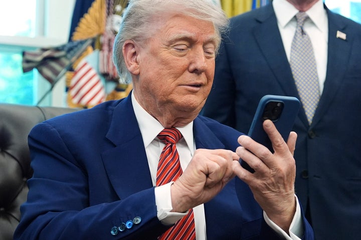 President Donald Trump looks at his mobile phone while speaking to reporters in the Oval Office of the White House on Friday, May 23, 2025. (AP Photo/Evan Vucci)