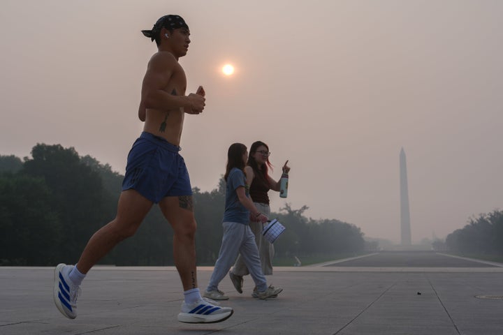 The sun is obscured by wildfire smoke as people run in front of the Washington Monument and Lincoln Memorial Reflecting Pool, Friday, July 17, 2026, on the National Mall in Washington. (AP Photo/Julia Demaree Nikhinson)