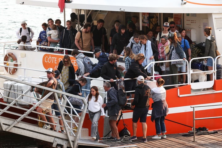 Holidaymakers from Lege-Cap-Ferret disembark from a boat upon their arrival in Arcachon during an evacuation operation of the entire Cap-Ferret peninsula, in southwestern France, on July 24, 2026 whilst a wildfire is spreading across the area.