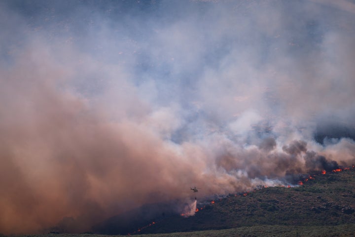 A firefighting helicopter drops water on the flames as a wildfire advances near Burgohondo, Ávila province, on July 24, 2026.