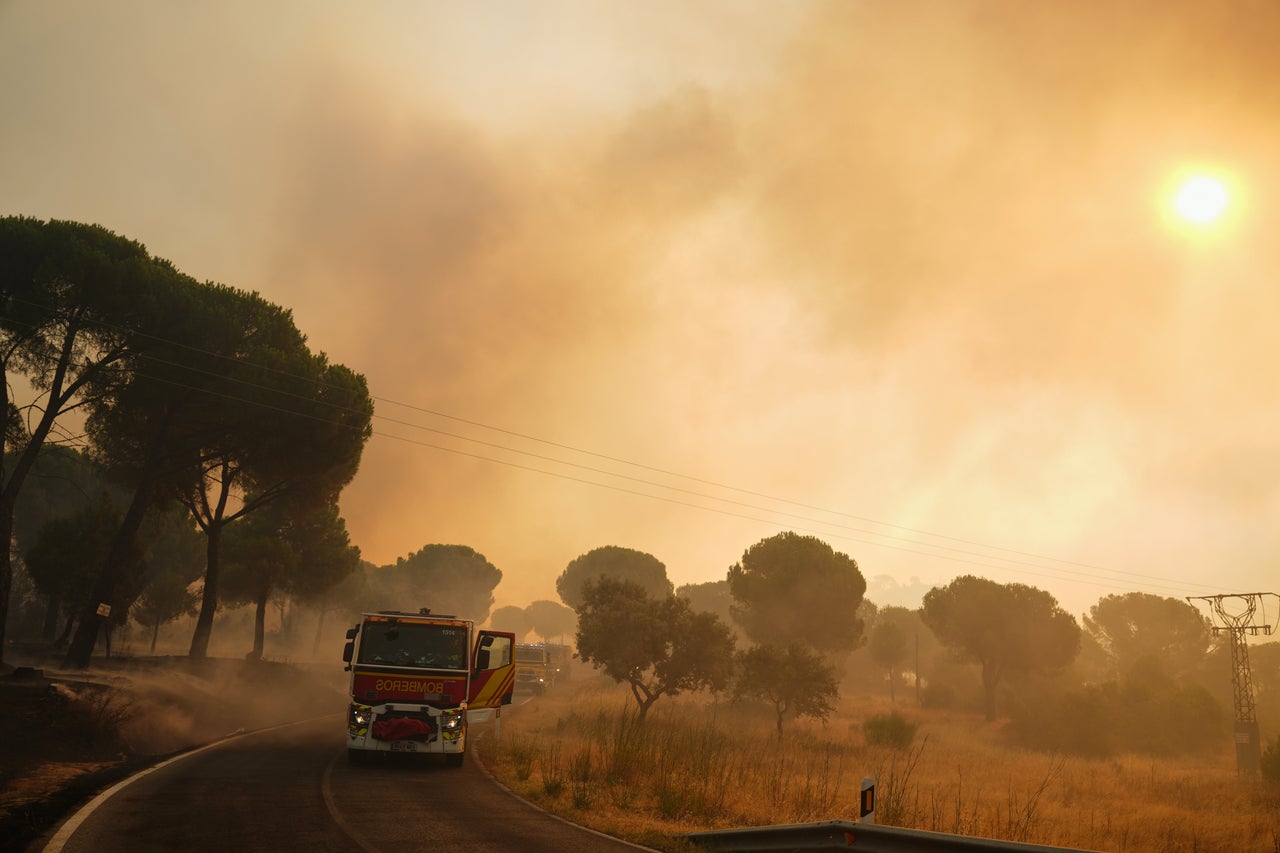 Fire trucks stand on the road as smoke rises from a forest fire in San Martin de Valdeiglesias, Spain, on July 26, 2026. 
