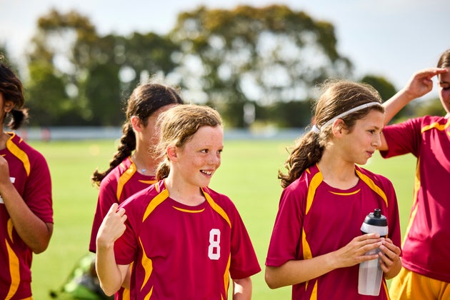 Smiling professional soccer players after session on field. Girls in sports jersey during break time. They are looking away.