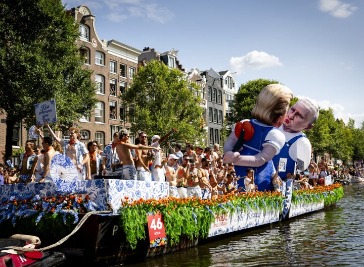 People stand on a boat next to giant inflatable puppets depicting Trump and Putin during the Canal Parade.