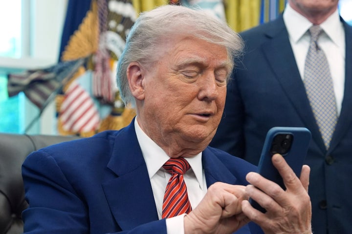 President Donald Trump silences his mobile phone which rang two times as he was speaking to reporters after signing executive orders regarding nuclear energy in the Oval Office of the White House, Friday, May 23, 2025, in Washington. (AP Photo/Evan Vucci)