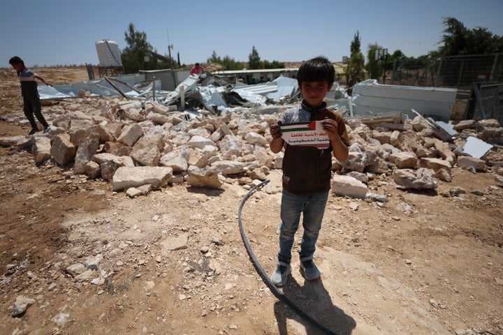 A child holds a sign near the rubble of Shaab al-Butum School, where Israeli forces demolished three classrooms, in Masafer Yatta, south of Hebron in the occupied West Bank on Aug. 4, 2026. The Palestinian Ministry of Education announced that the Israeli military had issued demolition orders against 14 schools in Masafer Yatta and surrounding areas, warning that the orders threaten the education of more than 1,500 primary and secondary students.