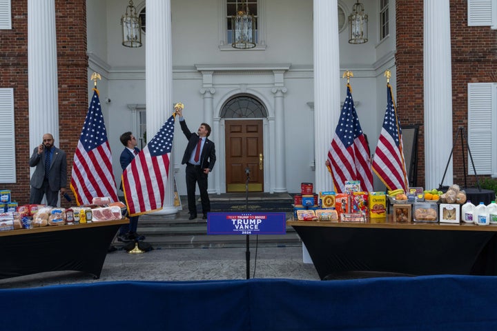 BEDMINSTER, NEW JERSEY - AUGUST 15: People adjust an American flag as groceries sit on a table before Republican presidential candidate, former U.S. President Donald Trump holds a news conference outside the Trump National Golf Club Bedminster on August 15, 2024 in Bedminster, New Jersey. (Photo by Adam Gray/Getty Images)