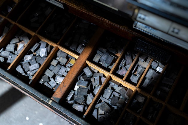 A close-up of open wooden drawers of metal typeface in storage at a printing press.