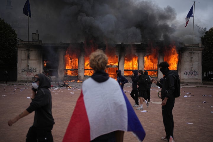 A protester wraps a French flag around them in front of the burning tourism office during a demonstration against rising living costs and in solidarity with students’ grievances in Lyon, France, Saturday, Oct. 17, 2026.(AP Photo/Laurent Cipriani)