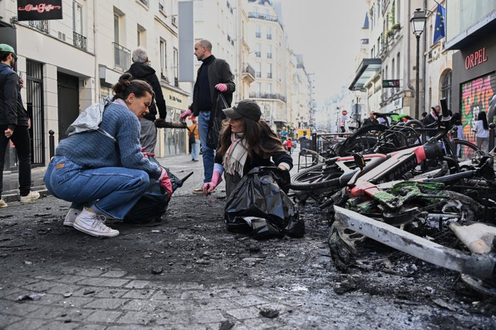 People clean up debris in a street next to burned bicycles the day after a demonstration against rising living costs and in solidarity with students' grievances, in Paris, Sunday, Oct. 18, 2026. (AP Photo/Emma Da Silva)