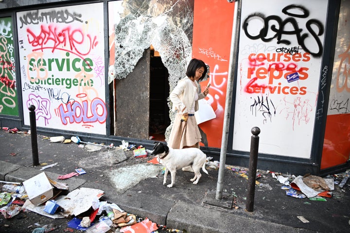 A woman walks her dog past a looted store the day after a demonstration against rising living costs, joining students' grievances, in Paris, Sunday, Oct. 18, 2026. (AP Photo/Emma Da Silva)