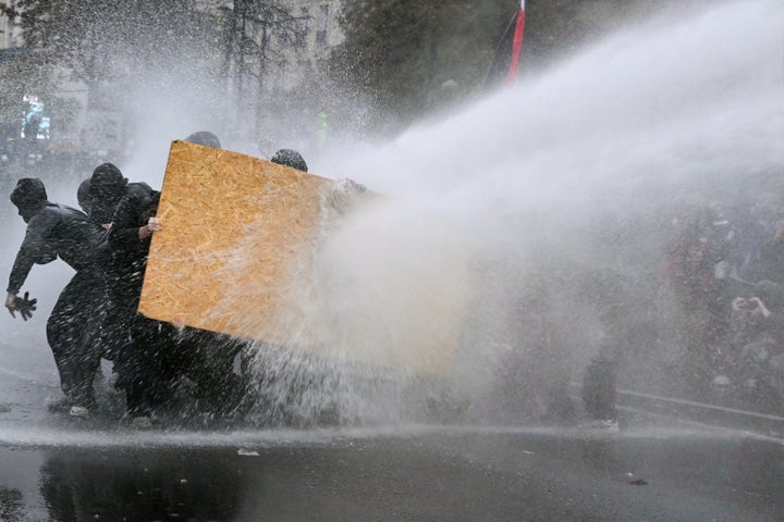 Protesters shelter from a police's water cannon near Porte de Vincennes during a demonstration in favor of purchasing power, the protection of public services, and fiscal and social justice, in Paris on October 24, 2026 as part of a nationwide call for mobilisation bringing together former members of the Yellow Vest movement, labor unions, high school and university students. (Photo by NICOLAS TUCAT / AFP via Getty Images)